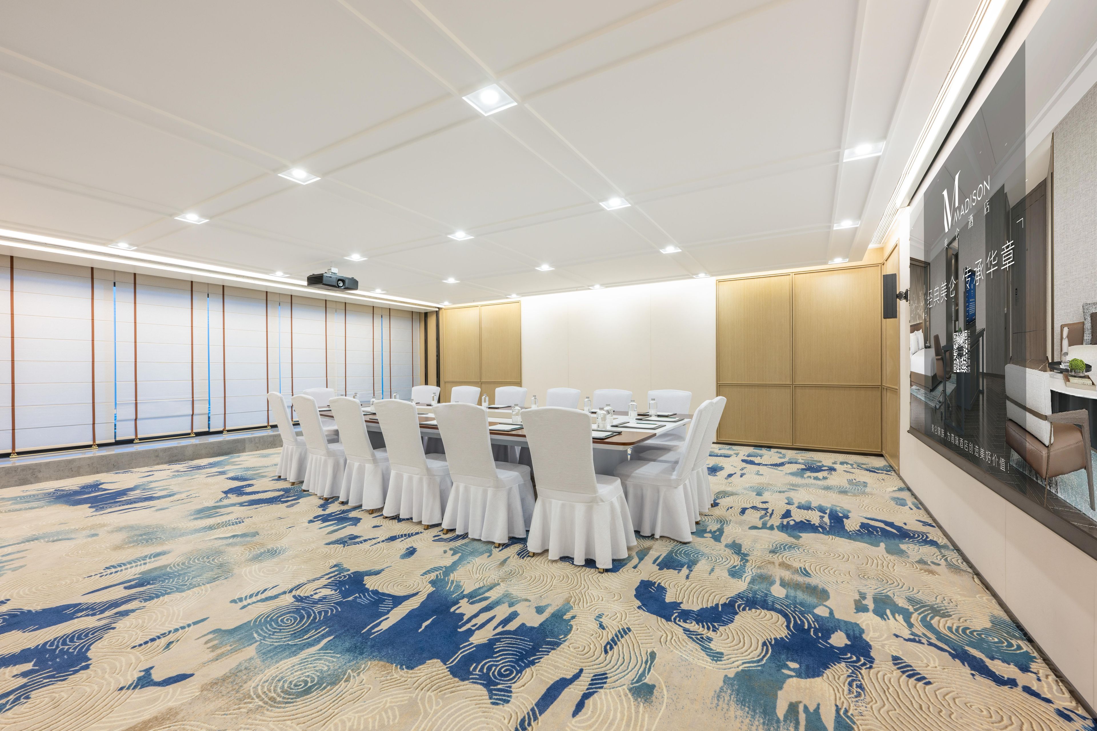 A conference room with a large table, white chairs, and a patterned carpet.