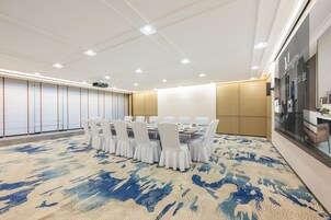 Un salón de conferencias con una gran mesa, sillas blancas y una alfombra estampada.