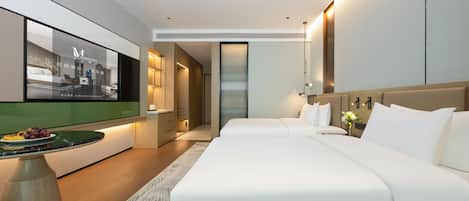 Una habitación de hotel moderna con una cama grande, un televisor en la pared, una mesita con una bandeja de fruta y una mesita de noche con una lámpara.