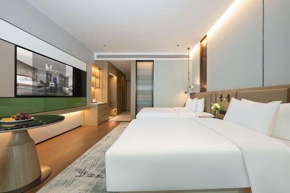 Una habitación de hotel moderna con una cama grande, un televisor en la pared, una mesita con una bandeja de fruta y una mesita de noche con una lámpara.