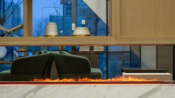 Una sala moderna con chimenea, un sofá verde y vistas de la ciudad a través de amplios ventanales.