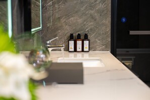 A bathroom with a marble sink, three bottles of hair care product, and a glass vase with flowers. - Madison Hotel Binzhou Bincheng Wanda Plaza (Binzhou)
