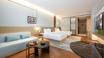 Una habitación de hotel moderna con sofá, cama, mesa de comedor con fruta y un espejo grande.