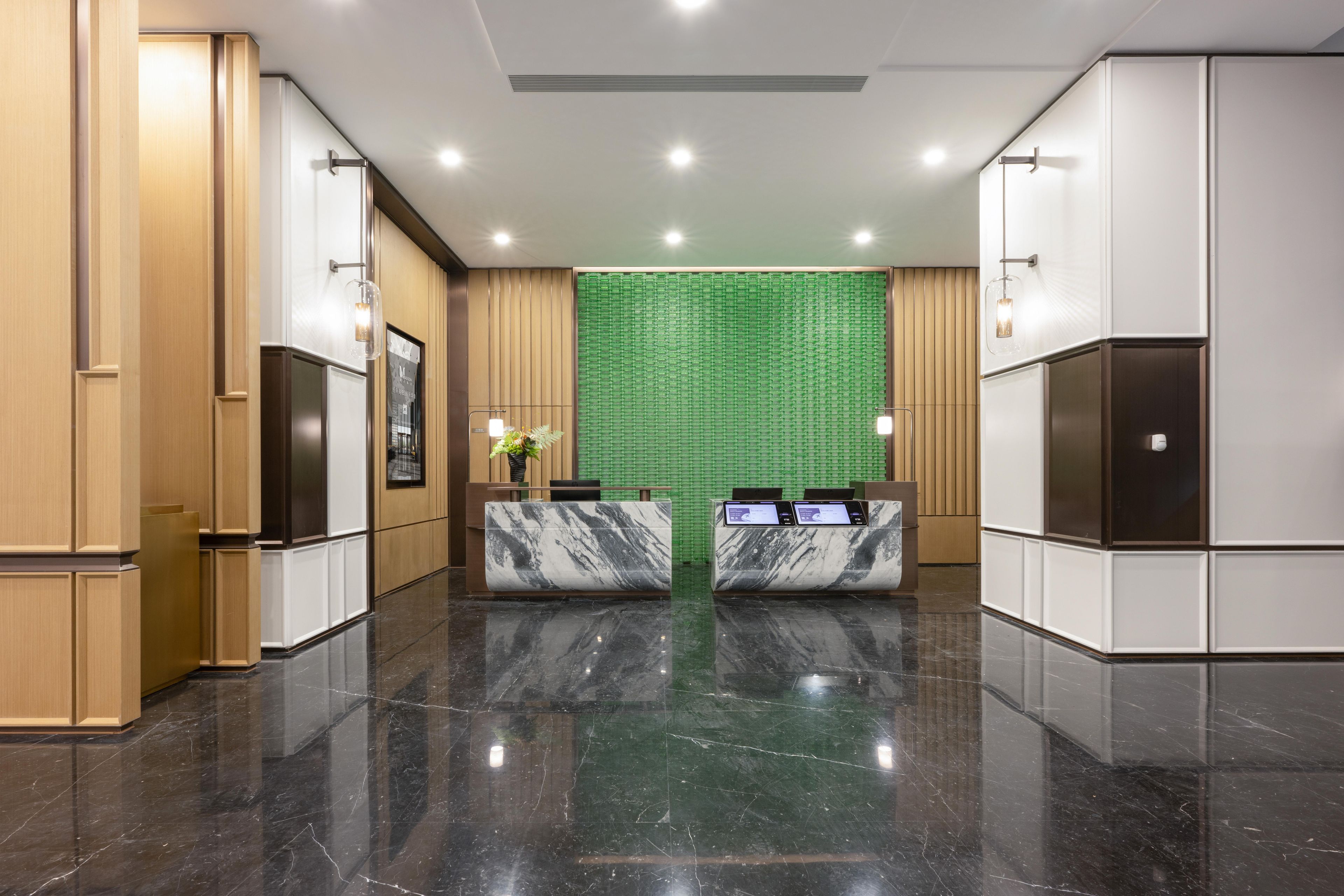 A modern hotel lobby with a marble reception desk, wooden paneling, and a green patterned wall.