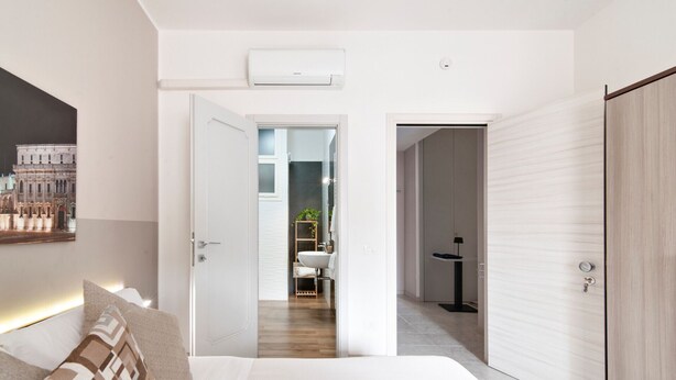 A hotel room with a bed, a bedside table, a wardrobe, and a bathroom visible through an open door.
