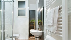 A modern bathroom with a glass shower enclosure, a toilet, a bidet, a sink with a mirror, and a towel rack.