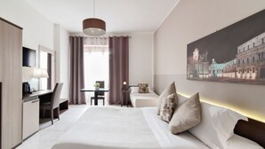 A hotel room with a bed, desk, chair, and a painting on the wall.