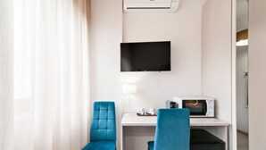 Ett hotellrum med ett skrivbord, två stolar, en platt-TV, en lampa, en mikrovågsugn och ett litet kylskåp.