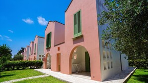 A row of pink buildings with green shutters, a paved walkway, and a well-maintained lawn. - Borgo Primizia B3 Pool And Sea, Otranto, Italy (Otranto)
