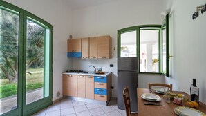 A kitchen with wooden cabinets, a sink, and a refrigerator. There is a dining table with chairs and plates. - Borgo Primizia B3 Pool And Sea, Otranto, Italy (Otranto)