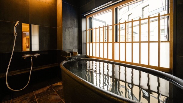 A modern bathroom with a large bathtub, a shower, and a window with a view of buildings. - Yukawa Terrace (Kusatsu)