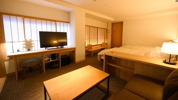 A hotel room with a bed, a desk with a television, a chair, a small table, and a bench.