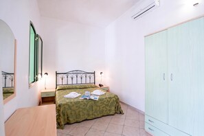 A bedroom with a bed, bedside tables, a wardrobe, a mirror, and an air conditioning unit.