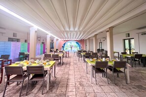 A dining area with multiple tables and chairs, a tiled floor, and a view through a semi-transparent archway.