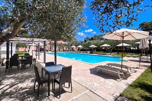 An outdoor pool area with lounge chairs and umbrellas, surrounded by a pergola and a poolside table.