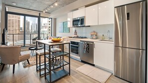 A modern kitchen with stainless steel appliances, a dining area with a bar stool, and large windows offering a city view.