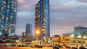 A high-rise building with multiple balconies, surrounded by other tall buildings and a busy street with cars.