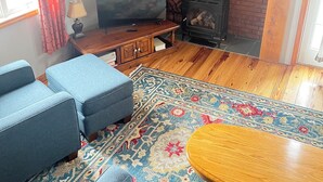 Una sala de estar con televisor, sofá, reposapiés, alfombra estampada y chimenea.