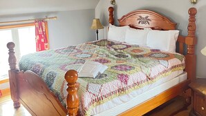 Un dormitorio con una cama de madera, una colcha acolchada, una mesita de noche, una lámpara y un cuadro en la pared.