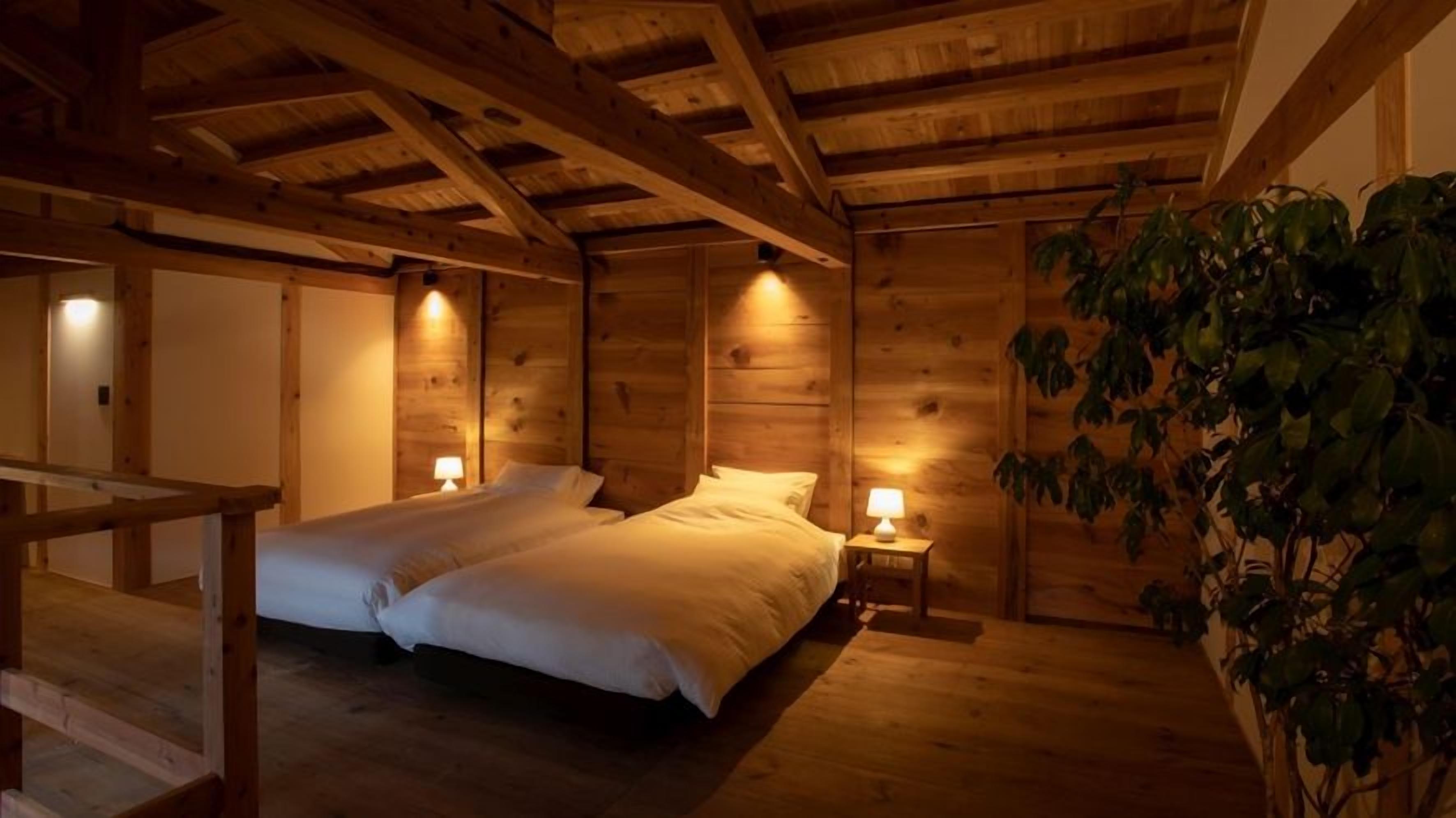 Una habitación tipo cabaña de madera con dos camas, una mesita de noche con lámpara y techo de madera.