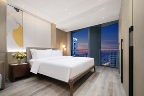 Een moderne hotelkamer met een groot bed, een nachtkastje met een bloevas en een stadsgezicht door grote ramen.