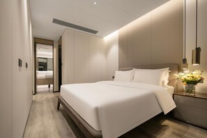 Een moderne hotelkamer met een groot bed, een nachtkastje met een bloevas, en uitzicht op de badkamer door een geopende deur.