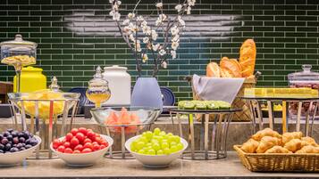 A buffet with various food items including fruits, pastries, and condiments.