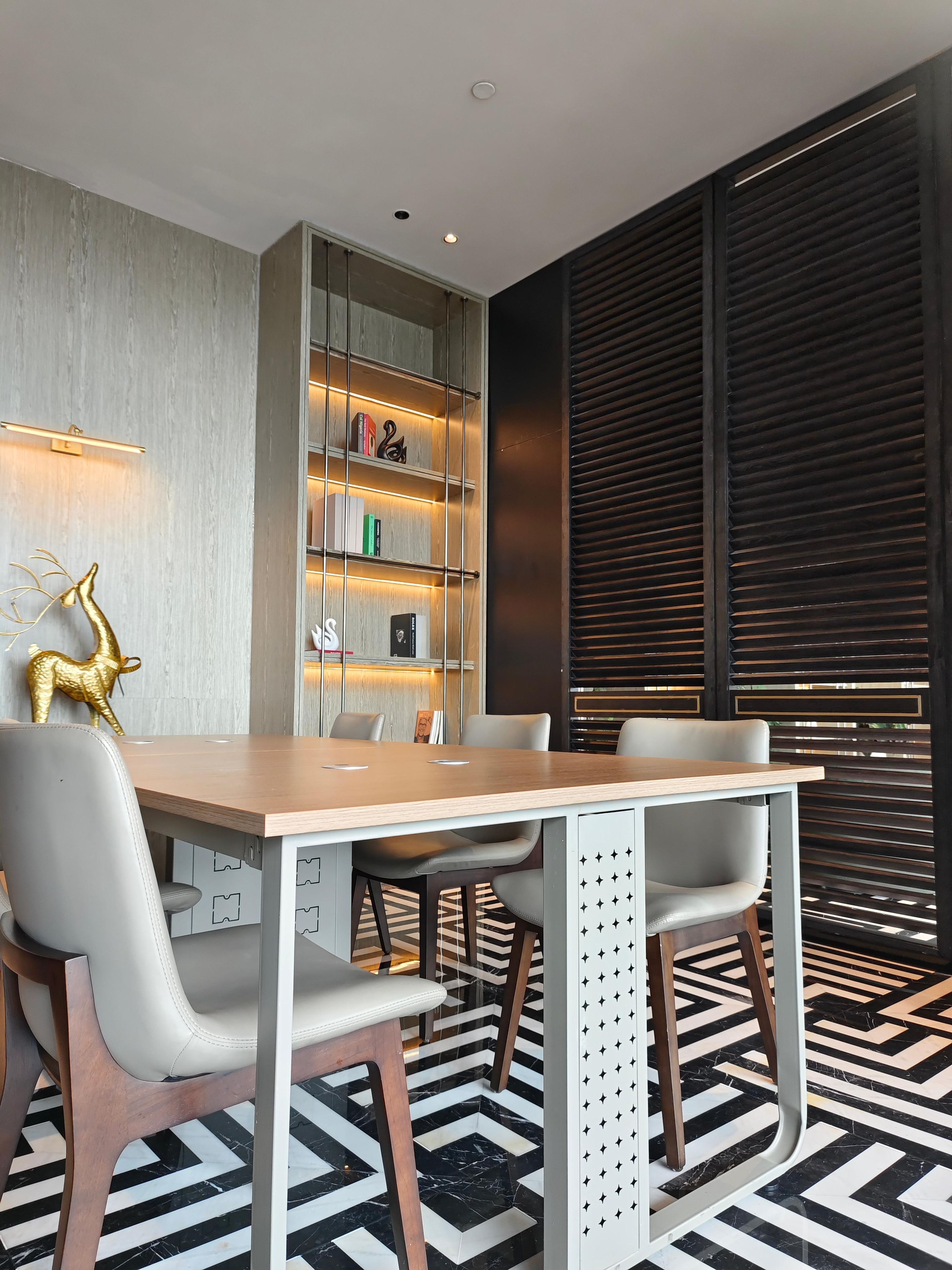 Uma área de refeições moderna com mesa de madeira, cadeiras brancas e uma girafa dourada decorativa.