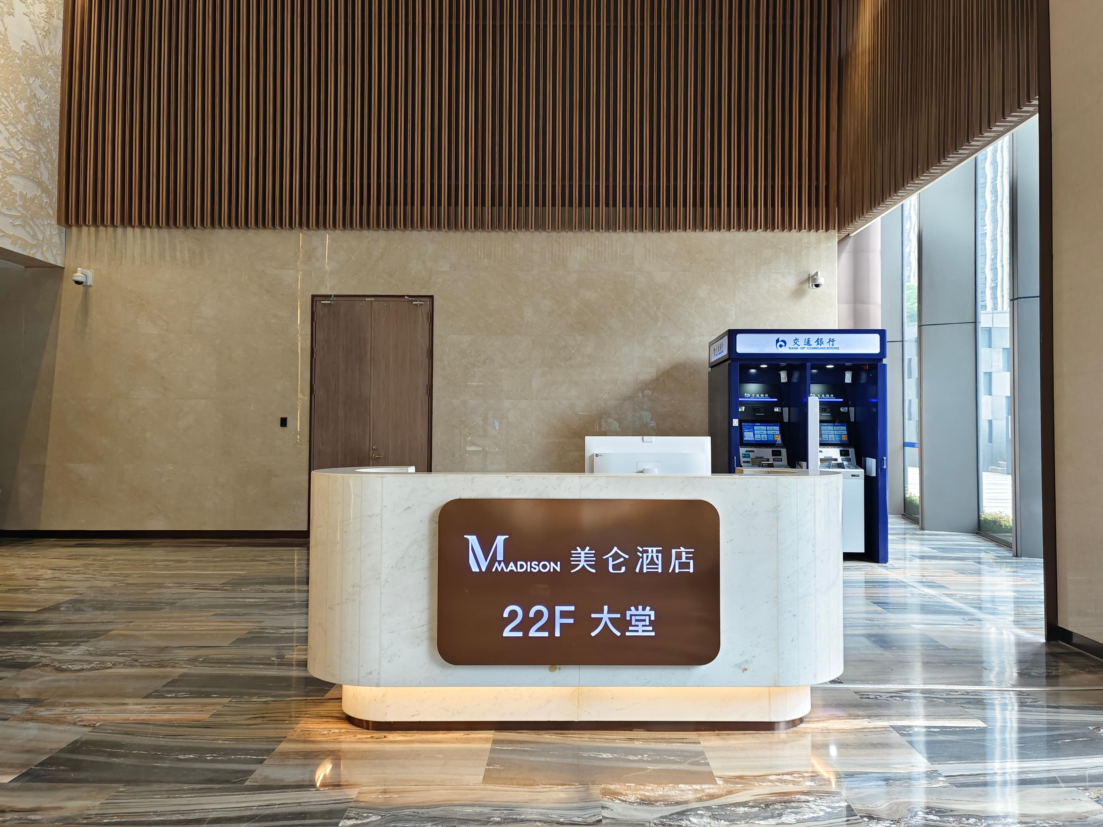 A reception desk with a sign indicating room number 22F in a hotel lobby with a modern design, a wooden slatted ceiling, and a blue ATM machine.