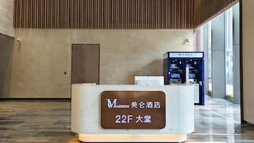 A reception desk with a sign indicating room number 22F in a hotel lobby with a modern design, a wooden slatted ceiling, and a blue ATM machine.