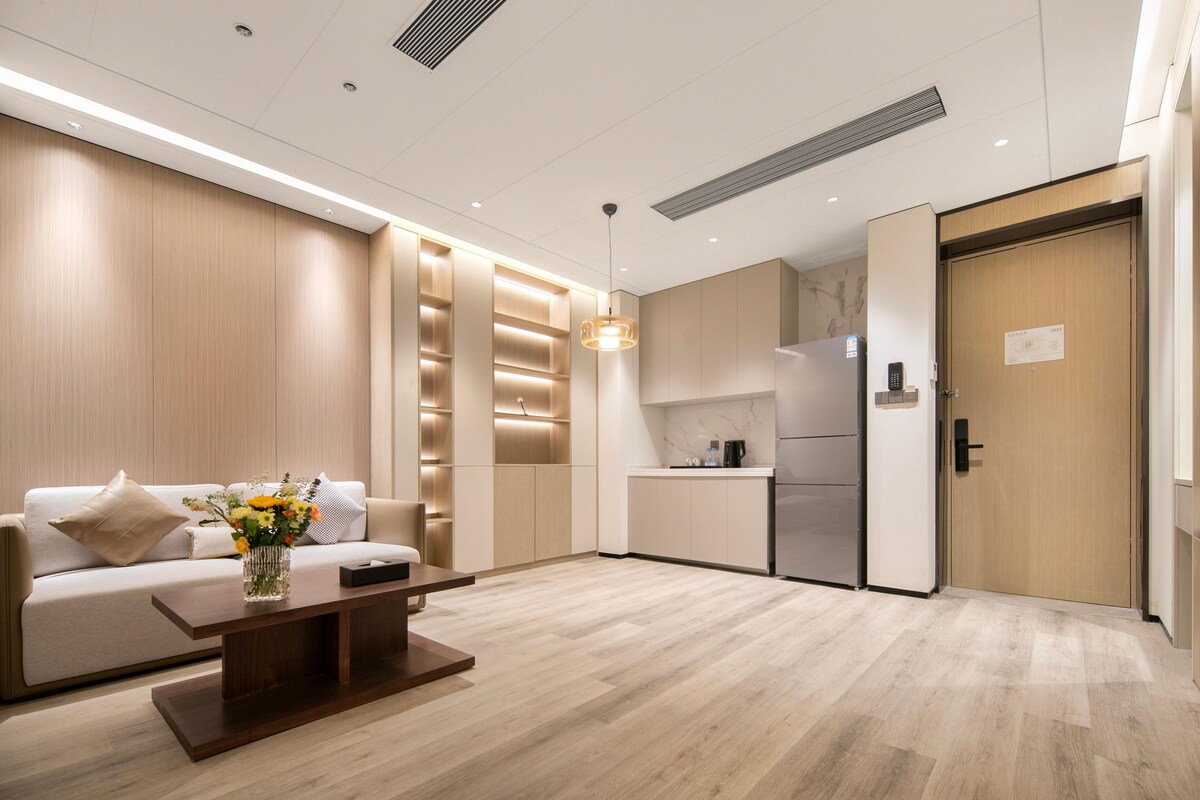 Een moderne hotelkamer met een bank, een salontafel, een kitchenette en een houten deur.