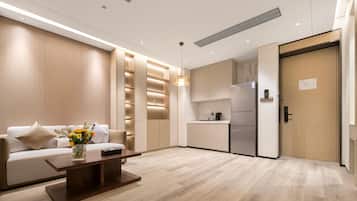 A modern hotel room with a sofa, a coffee table, a kitchen area, and a wooden door.
