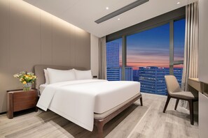 Ein modernes Hotelzimmer mit einem großen Bett, einem Schreibtisch und Blick auf eine Stadtlandschaft bei Sonnenuntergang.