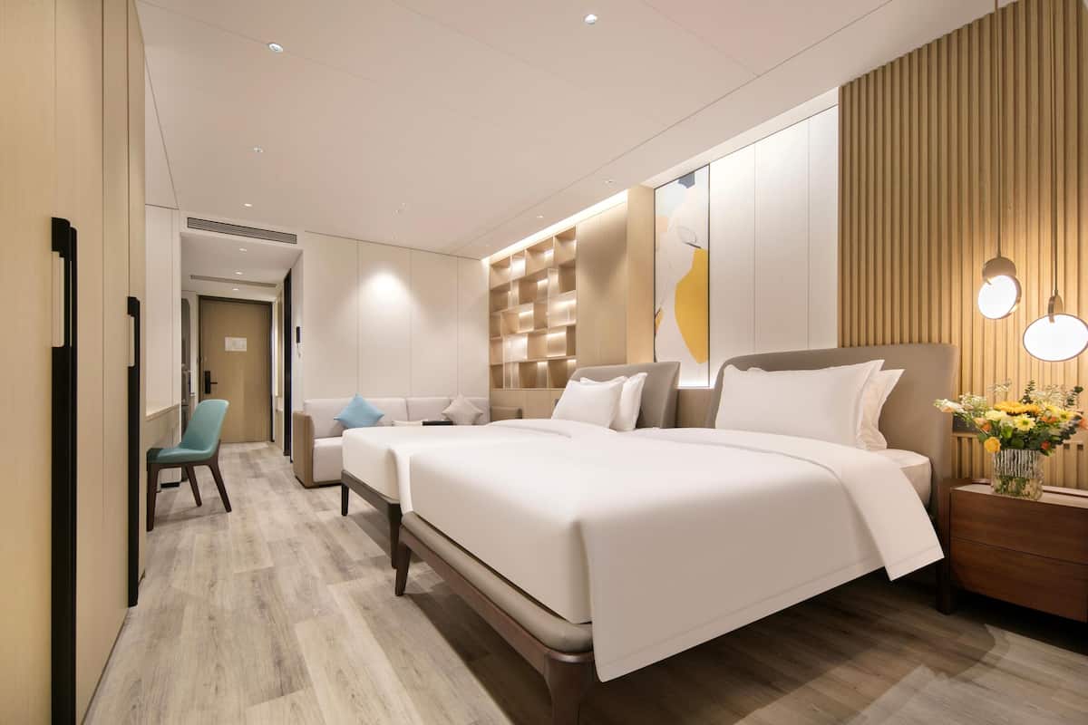 Ein Hotelzimmer mit einem großen Bett, einer Couch, einem Sessel und einem Nachttisch mit Blumen in einer Vase.
