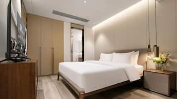 A modern hotel room with a large bed, a wooden desk, a TV, and a nightstand with a vase of flowers.