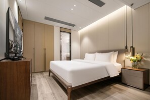 Une chambre d’hôtel moderne avec un grand lit, un bureau en bois, une télévision et une table de chevet agrémentée d’un vase de fleurs.