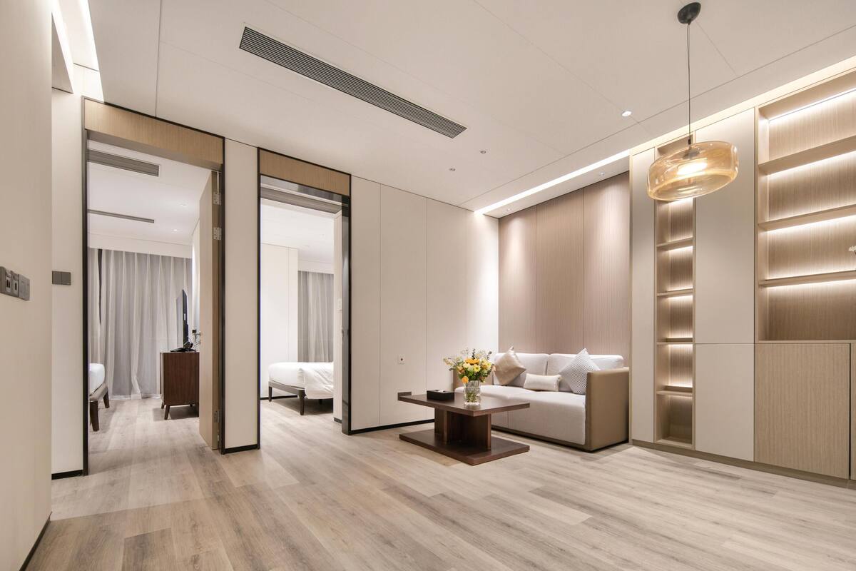 Ein modernes Hotelzimmer mit Holzboden, einer Couch, einem Couchtisch mit Blumen und einem großen Spiegel.