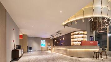 A modern hotel lobby with a curved reception desk, a digital screen, and a staircase.