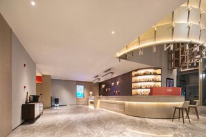 Eine moderne Hotelhalle mit einer gebogenen Rezeption, einem digitalen Bildschirm und einer Treppe.