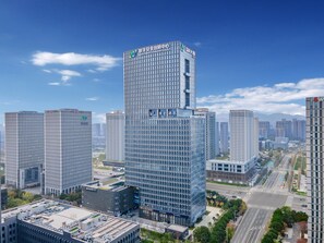 Ein modernes Hochhaus mit einer rasterförmigen Fassade, umgeben von weiteren Hochhäusern in einer Stadtansicht.