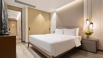 A modern hotel room with a large bed, bedside tables, a TV, and a wooden wardrobe.
