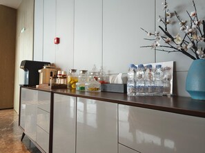Een receptiegedeelte met een balie, waterflesjes, een koffieapparaat en een vaas met takken.