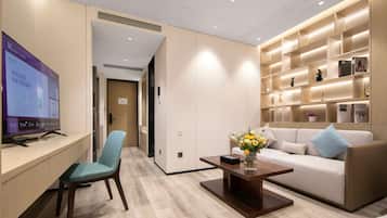 A modern hotel room with a wooden desk, a comfortable sofa, a coffee table, and a TV.