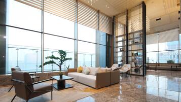 A spacious lobby with a modern sofa, armchairs, and a coffee table. Large windows provide natural light and a view of the city.