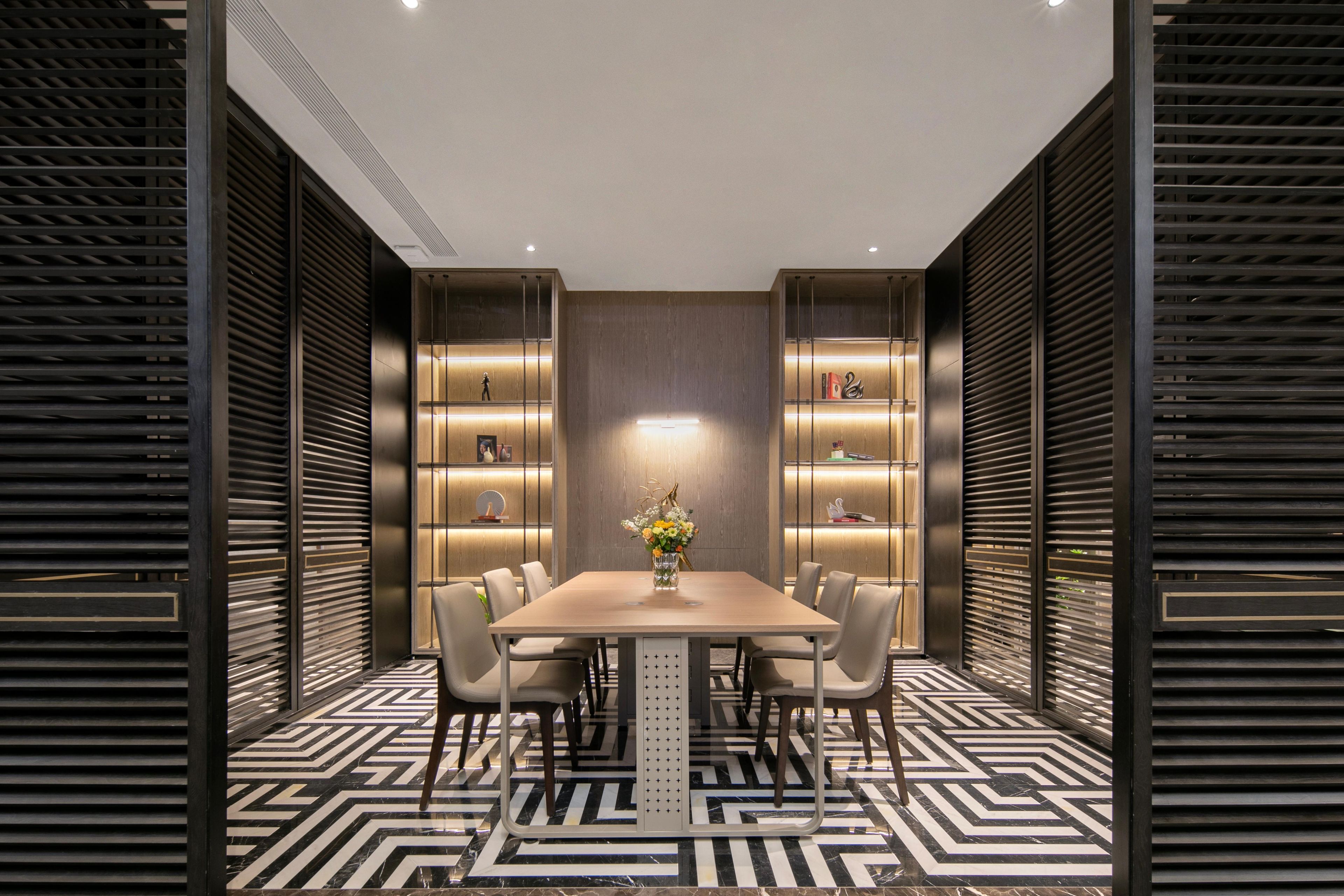 A modern dining area with a rectangular table, six chairs, and a vase of flowers.