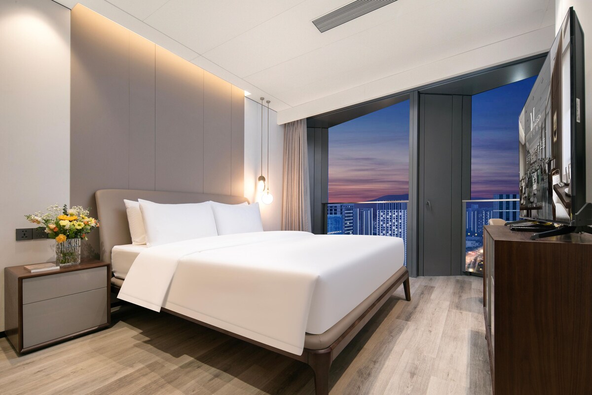 Een moderne hotelkamer met een groot bed, een bureau en uitzicht op de stad door een open deur.