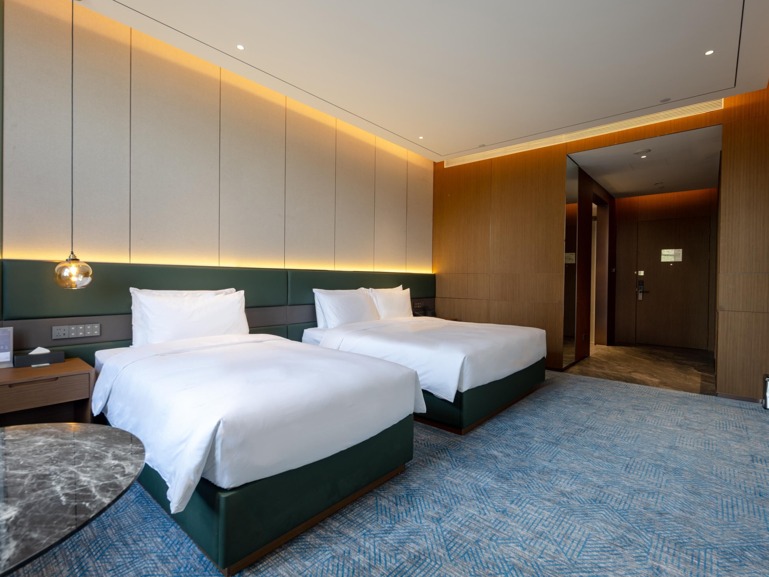 Quarto de hotel com duas camas, uma mesa de mármore e um tapete estampado.