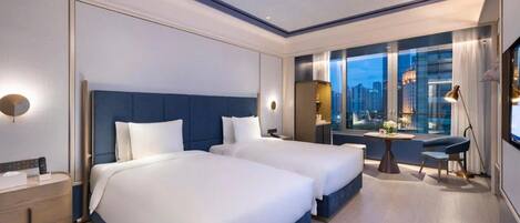 A modern hotel room with two beds, a city view, a desk, and a nightstand.