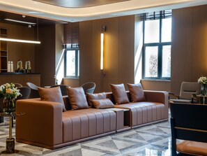 Un hall d’hôtel moderne avec un canapé en cuir marron, un comptoir d’accueil et de grandes fenêtres.