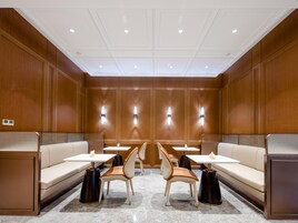 Un moderno vestíbulo de hotel con paneles de madera, un área de estar central con sofás y sillones, y mesas.